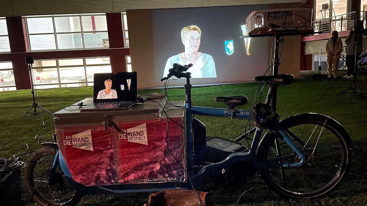 Ein Beamer projiziert ein Video einer Frau auf eine große Leinwand.
