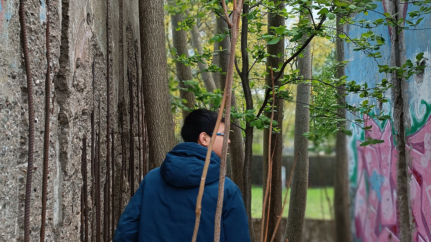 Eine Person steht zwischen zwei Mauerstücken in einem Wald.