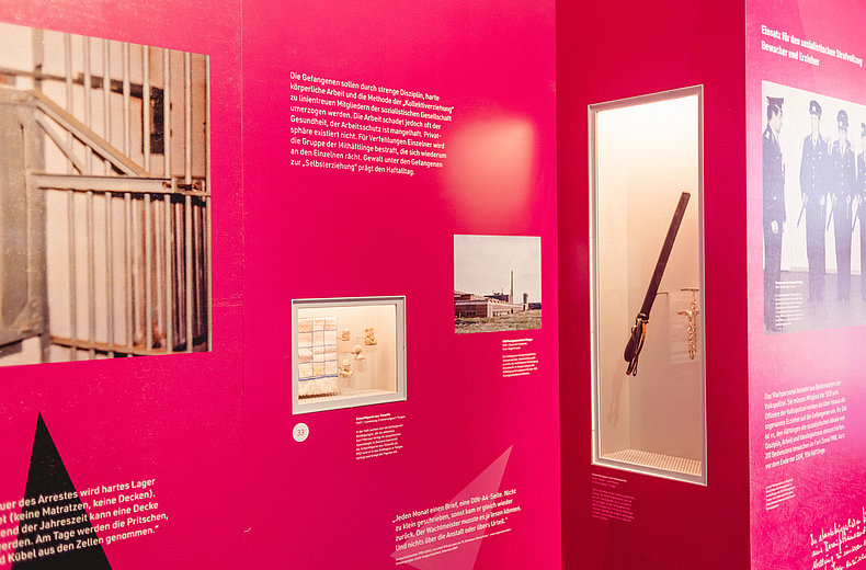 Eine rote Ausstellungswand mit mehreren Bildern und Texten.