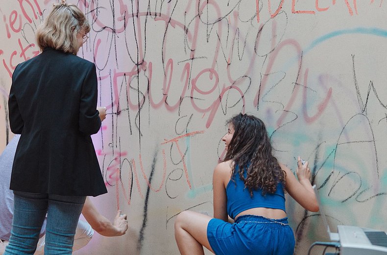Zwei junge Menschen malen Graffiti an eine Wand.