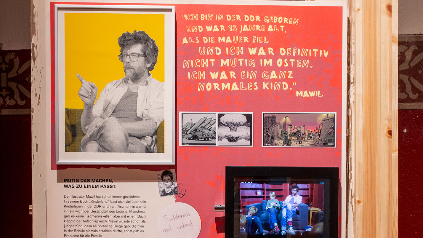 Eine Ausstellungsinfotafel mit Bildern und Video-Bildschirmen.