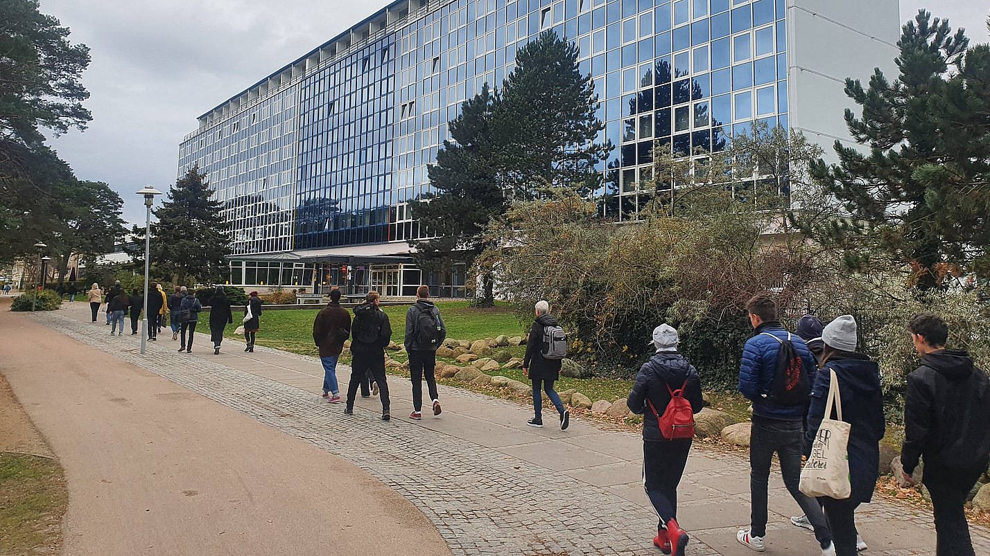Viele Menschen laufen einen Weg vor einem großen Gebäude entlang.
