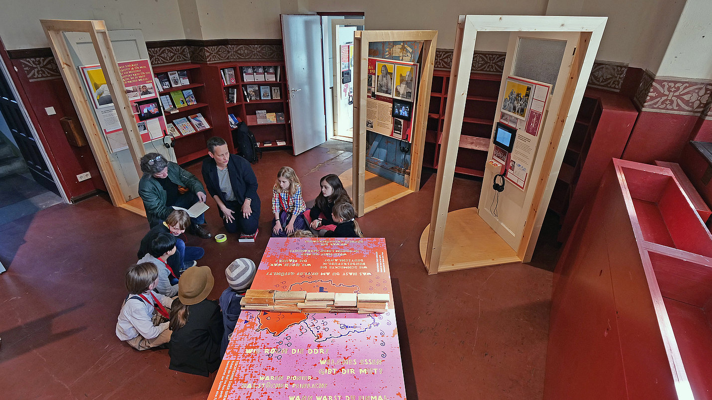 In der Ausstellung sitzen Kinder und Erwachsene in einem Kreis auf dem Boden.