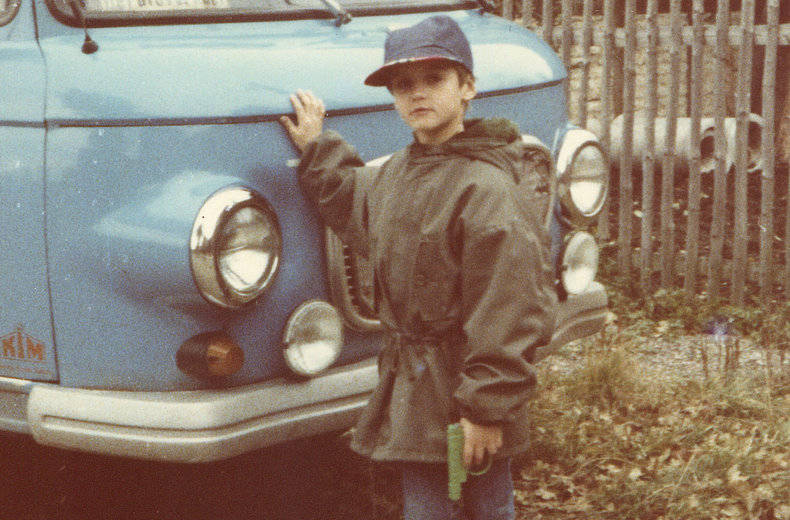 Ein Junge vor einem blauen Auto.